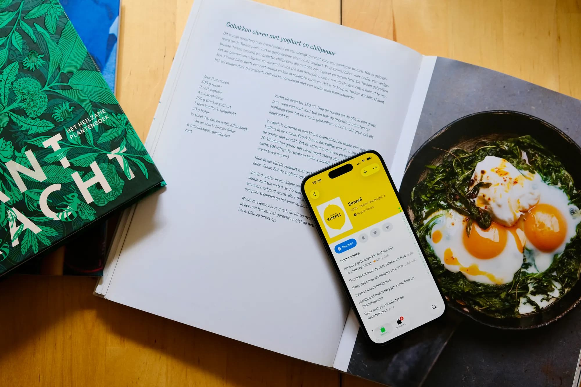 An iPhone showing Ottolenghi’s Simpel in CookCook, resting on an open cookbook beside a photo of fried eggs