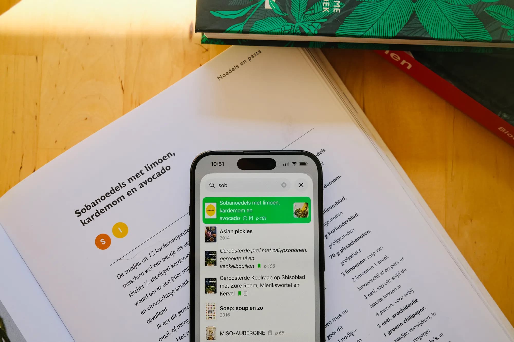 An iPhone searching CookCook for soba noodles, lying on the open cookbook the recipe comes from